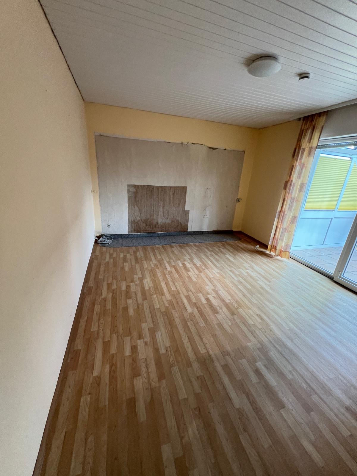 Ein leerer Raum mit Laminatboden und teilweise abgerissener Tapete an einer Wand