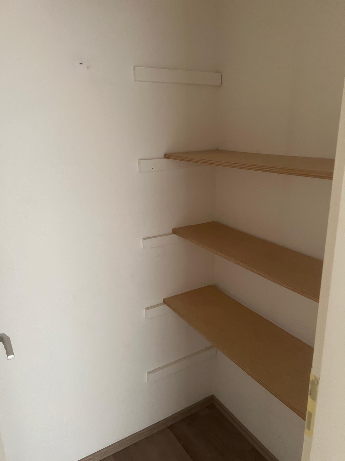 Drei Holzregale in einem schlichten, leeren weißen Raum.
