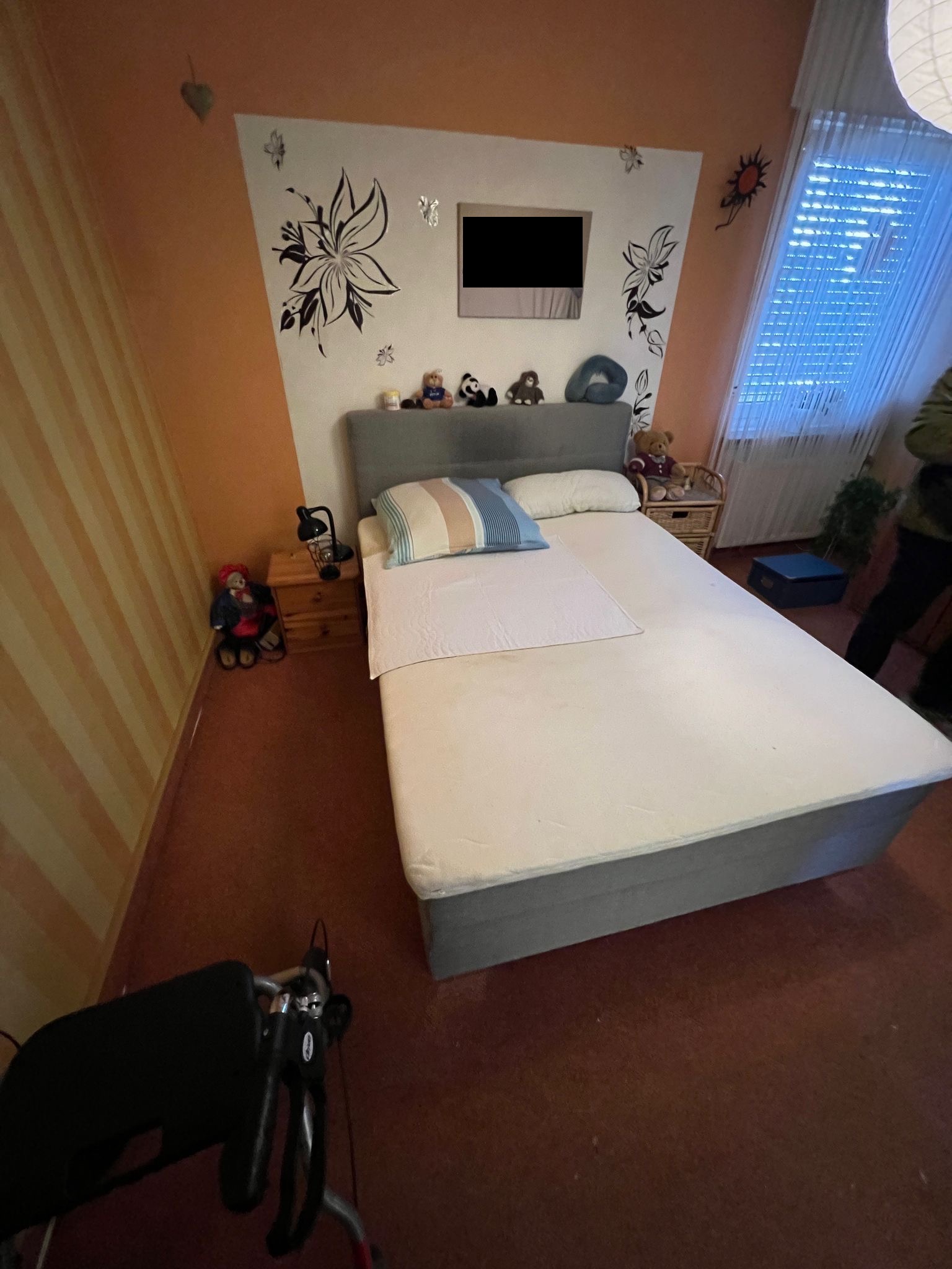 Ein gemütliches Schlafzimmer mit einem grauen Bett, gemusterten Wandtattoos und Kuscheltieren auf dem Kopfteil.
